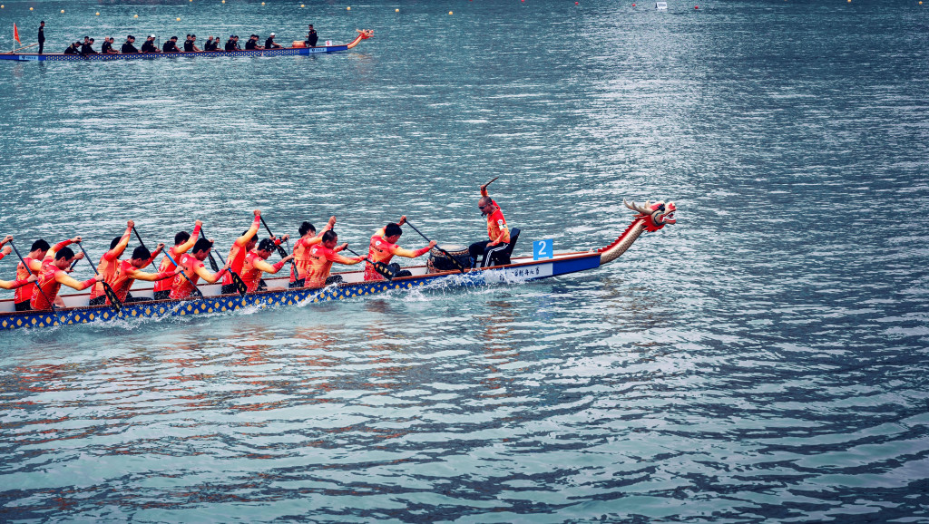 paddlers propel a dragon boat through blue wavy water from a distance