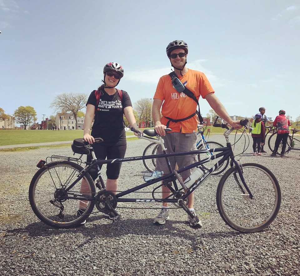 2 cyclists wearing helmets standing with tandem bike outdoor park