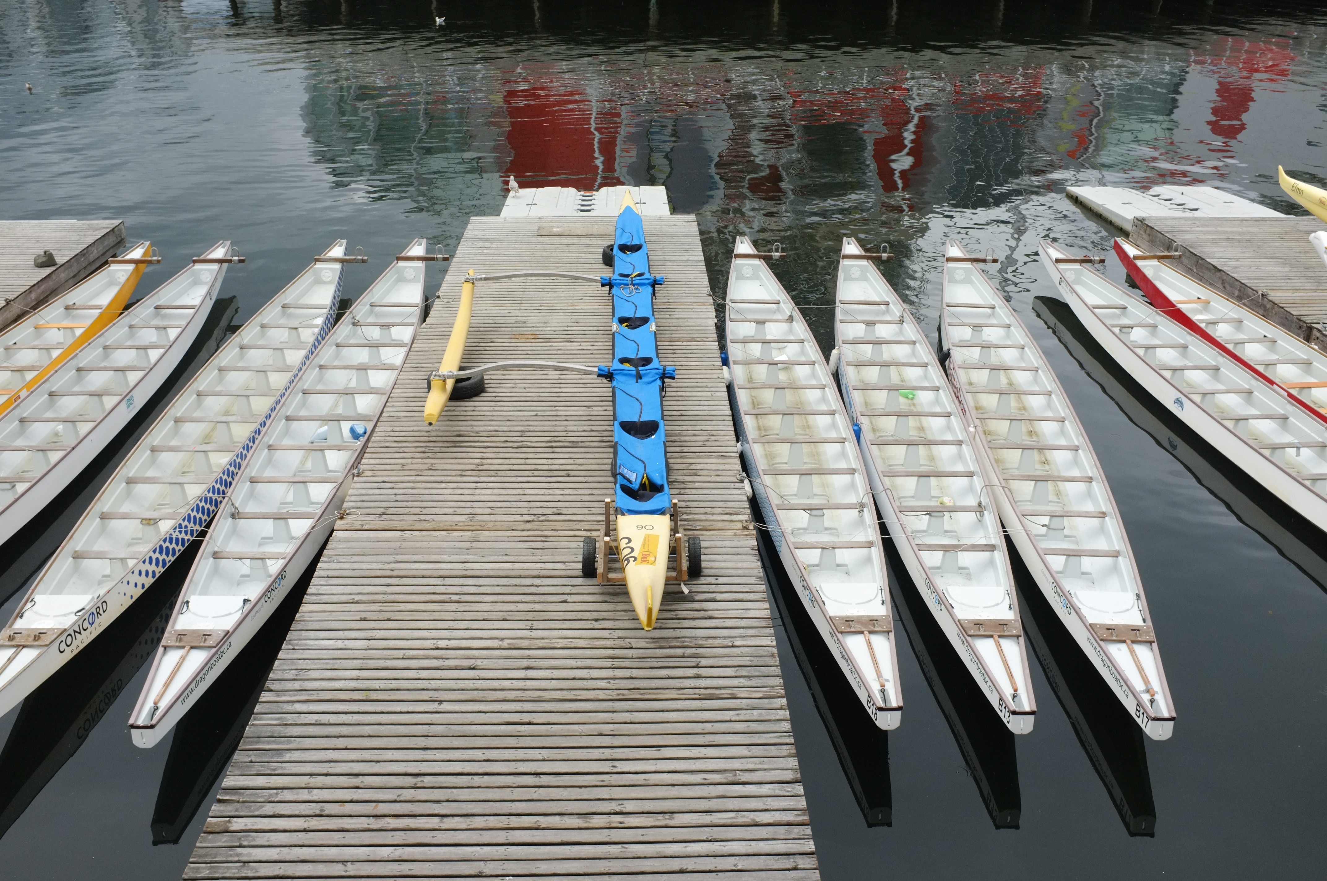 9 long dragon boats sitting empty in the water next to a dock