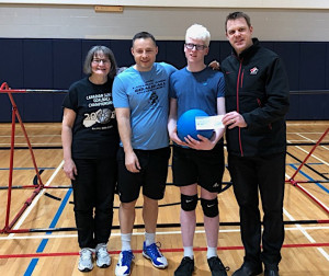 4 people in gymnasium holding goalball and cheque