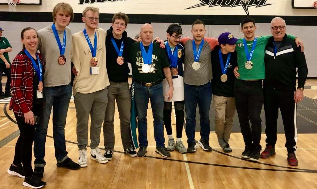7 people standing in a gymnasium wearing medals 