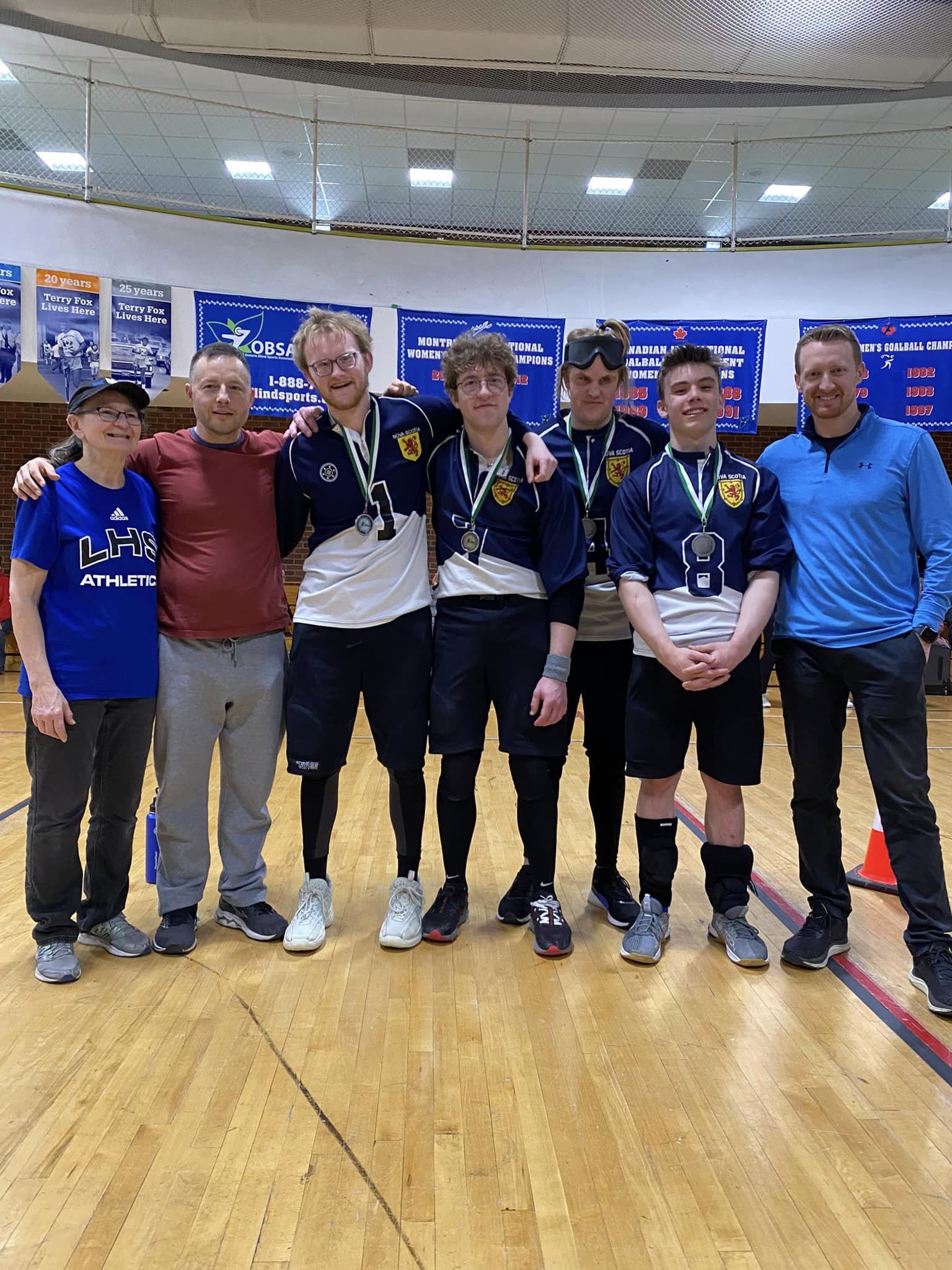 A group of people in a gymnasium wearing silver medals. They're smiling proudly.