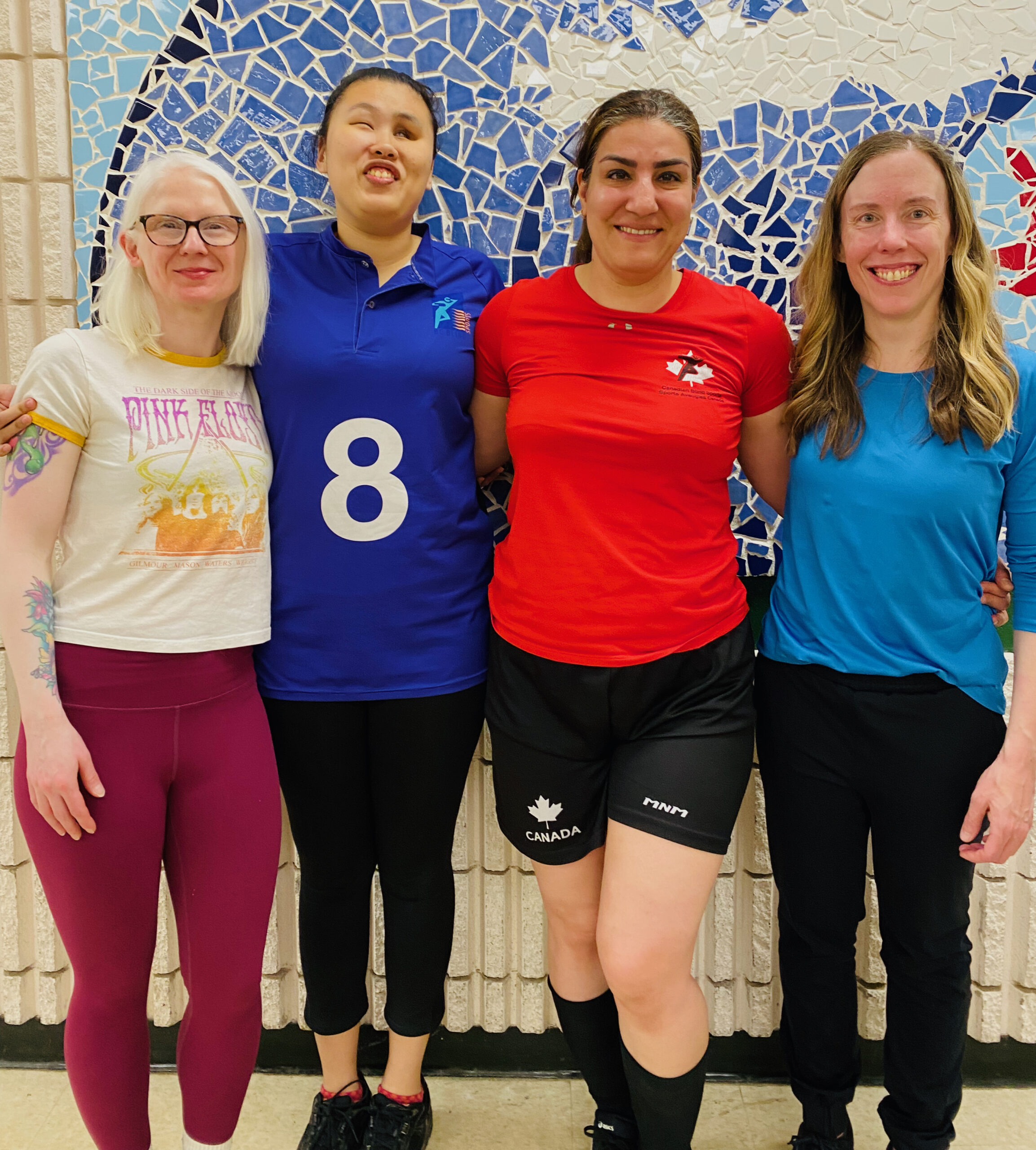 Four women stand shoulder to shoulder with arms around one another, smiling proudly