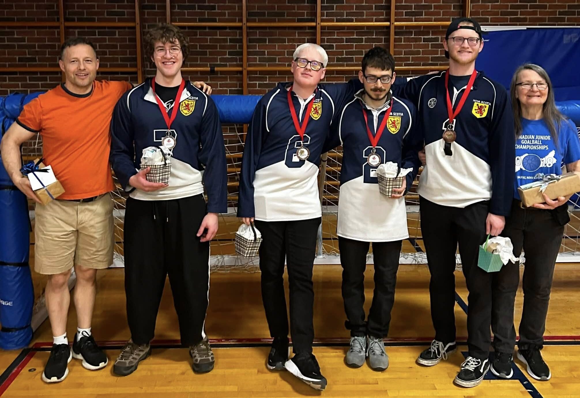 6 people wearing bronze medals standing in front of a goalball net